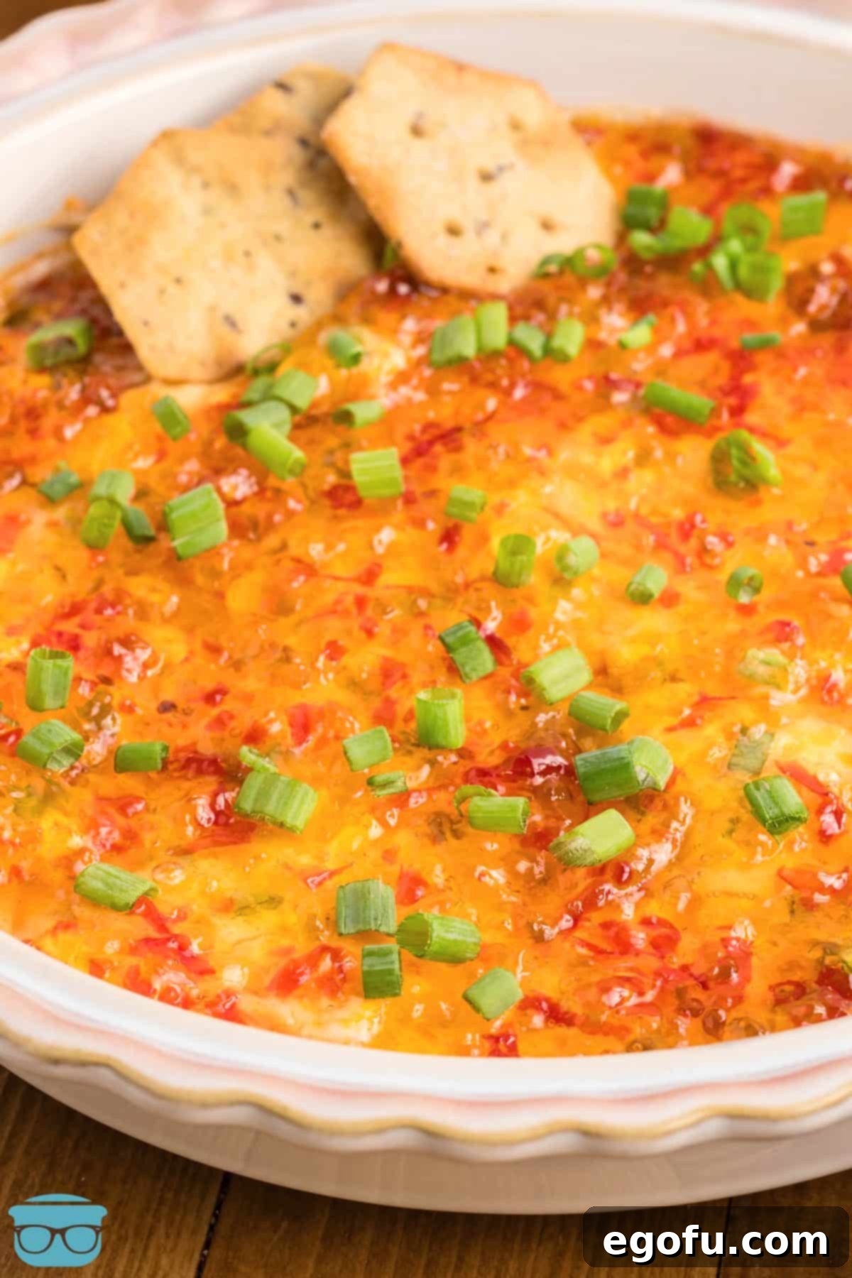 A few crackers poised in a bowl of Pepper Jelly Cream Cheese dip, showcasing its creamy texture and vibrant pepper jelly topping.