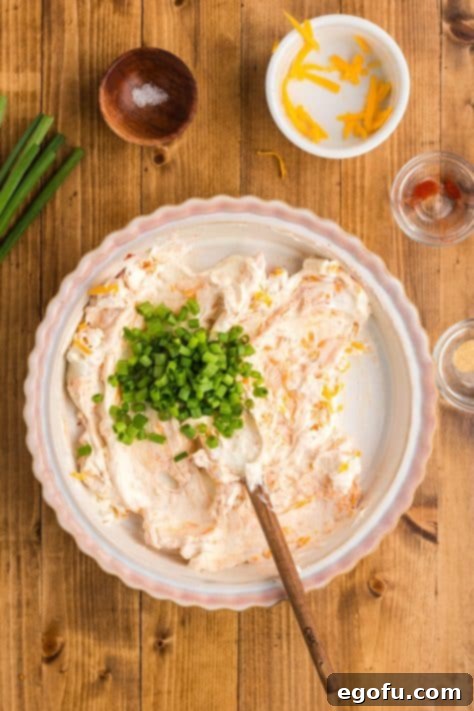 Fresh green onions being added to the cream cheese mixture, ready to be incorporated for added flavor.