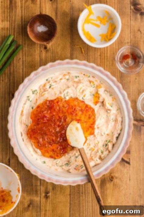 The warmed pepper jelly being smoothly spread over the cream cheese mixture, creating a glossy, inviting top layer.