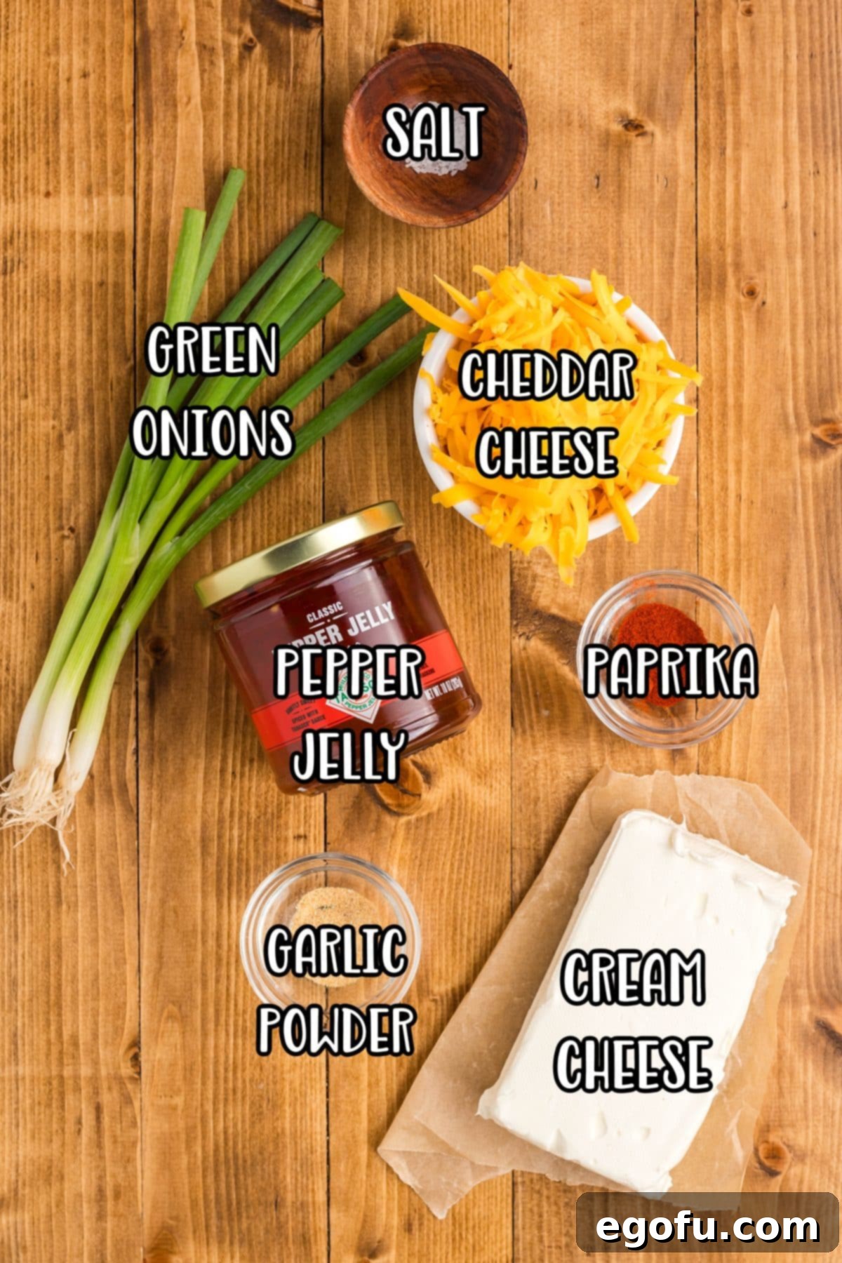 All the key ingredients for Pepper Jelly Cream Cheese: fresh green onions, shredded cheddar cheese, a jar of vibrant pepper jelly, a dash of paprika, aromatic garlic powder, a block of creamy cream cheese, and a pinch of salt, artfully arranged for preparation.