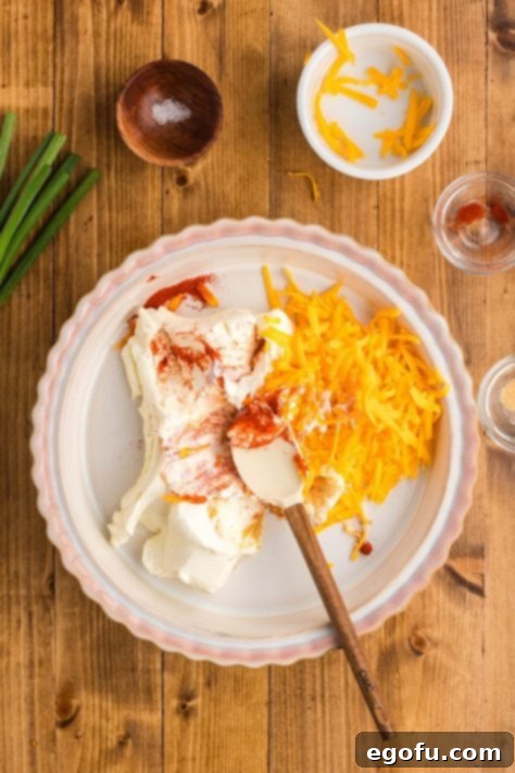 A pie plate with cream cheese, cheddar cheese, garlic powder, paprika, and salt mixed together, forming the base of the dip.