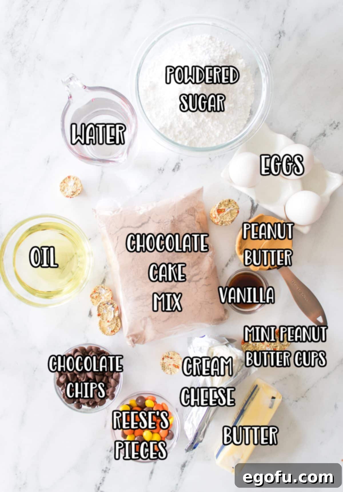 Assortment of ingredients for Peanut Butter Earthquake Cake: chocolate cake mix, powdered sugar, water, oil, eggs, peanut butter, vanilla extract, mini peanut butter cups, cream cheese, butter, Reese's Pieces, and chocolate chips.