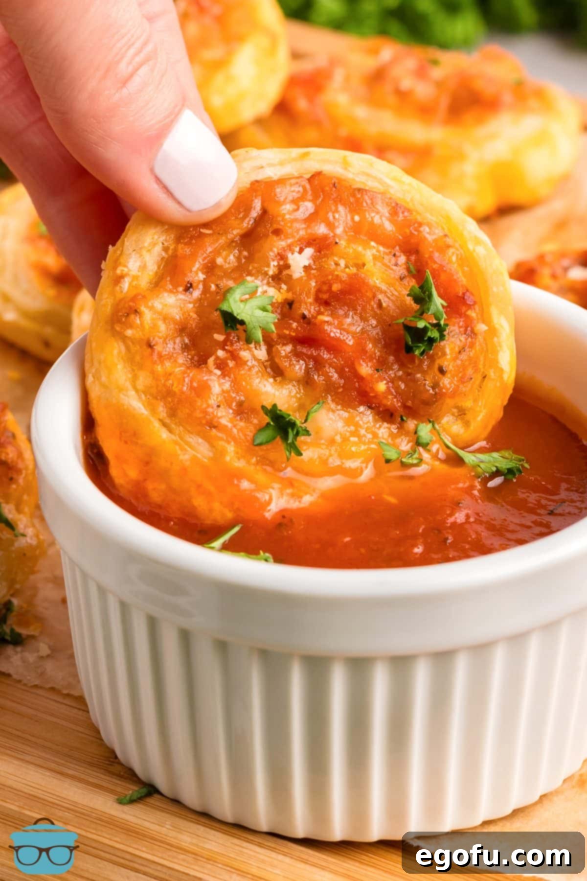 A hand reaches in to dip a warm, baked Pepperoni Pinwheel into a small ramekin of marinara sauce.