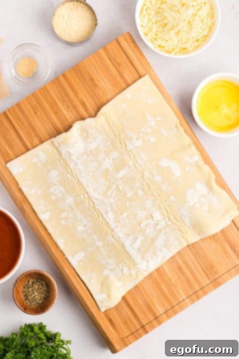 A sheet of puff pastry, rolled out flat on a wooden board.