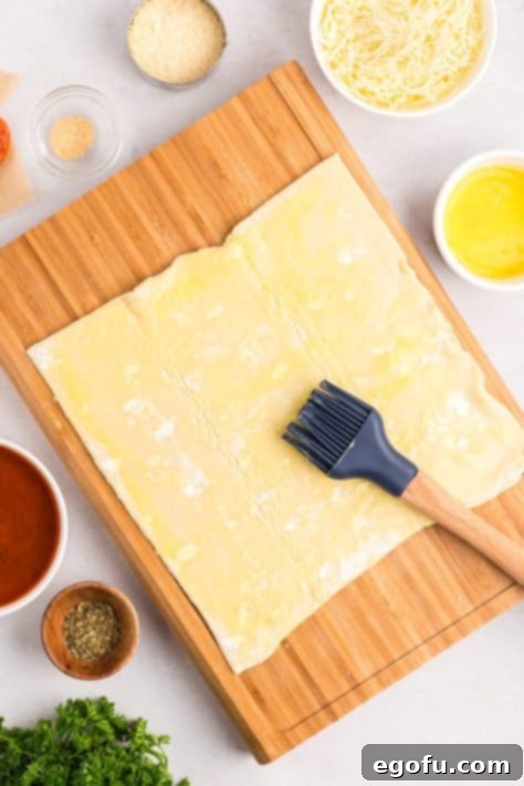 A pastry brush applying egg wash to a sheet of puff pastry.