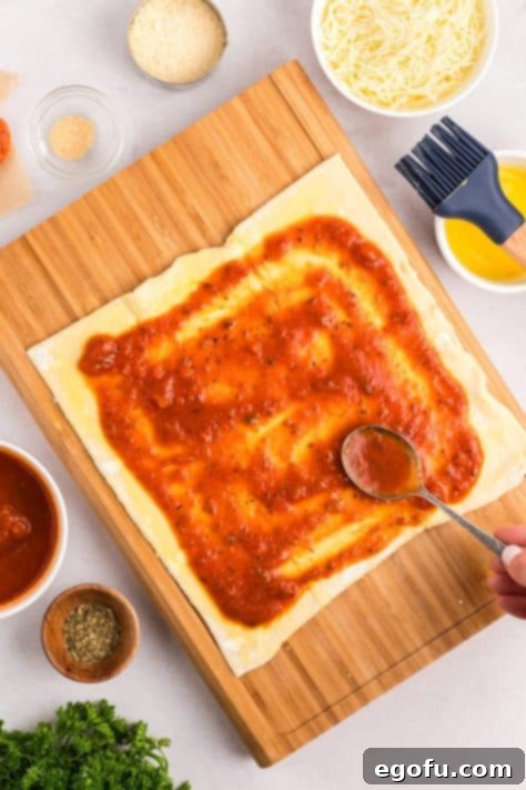 Marinara sauce spread on puff pastry, leaving a clean border.