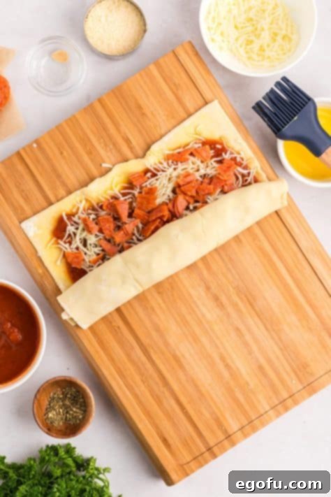 A sheet of puff pastry with toppings being rolled up tightly.