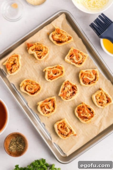 Sliced pepperoni pinwheels arranged on a parchment-lined baking sheet.