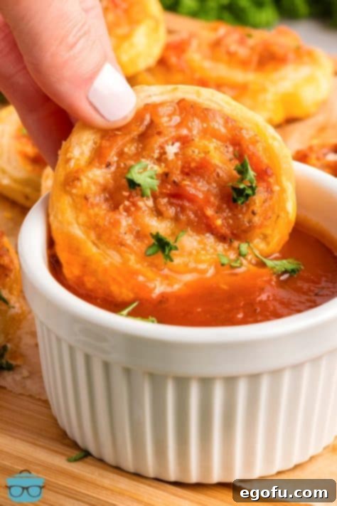 A hand dipping a Pepperoni Pinwheel in a ramekin of sauce.