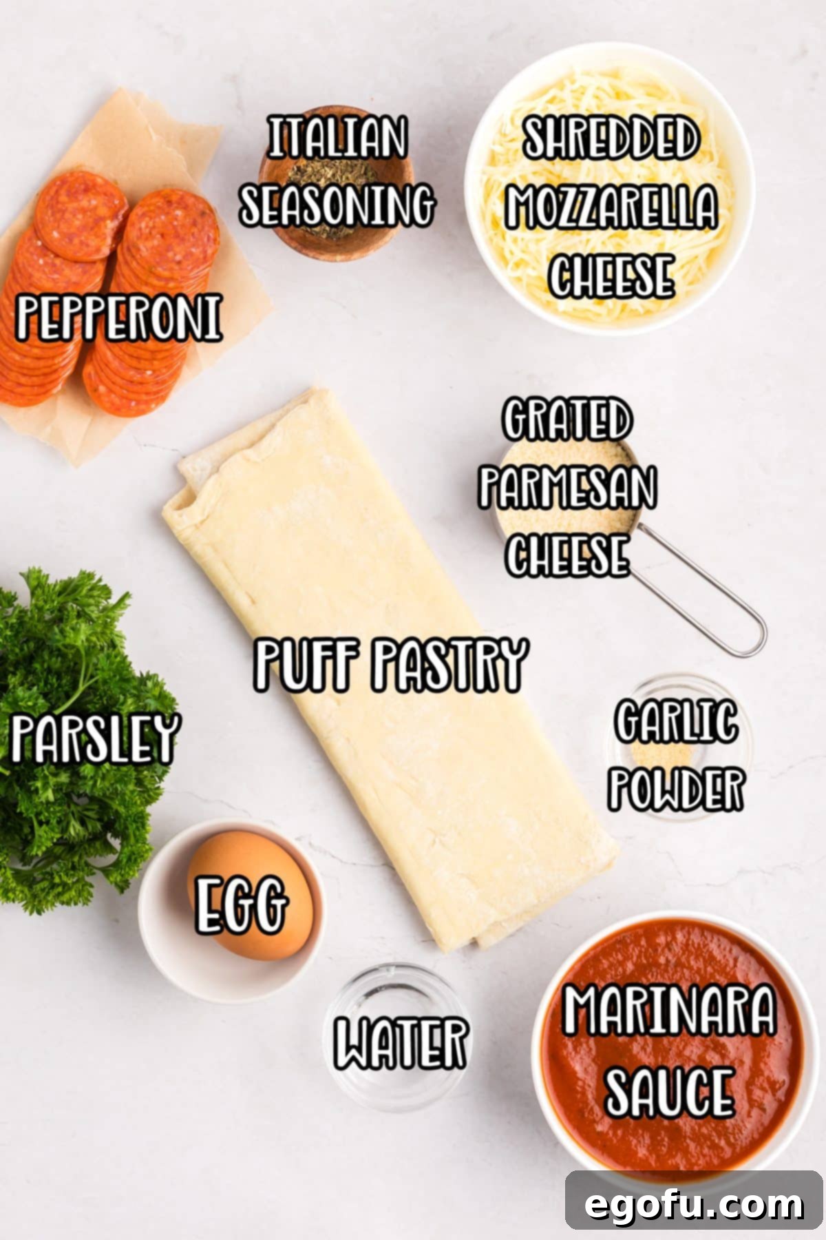 Individual ingredients neatly arranged: pastry sheets, egg, water, marinara sauce, shredded mozzarella cheese, Italian seasoning, pepperoni, garlic powder, grated parmesan, and fresh parsley.