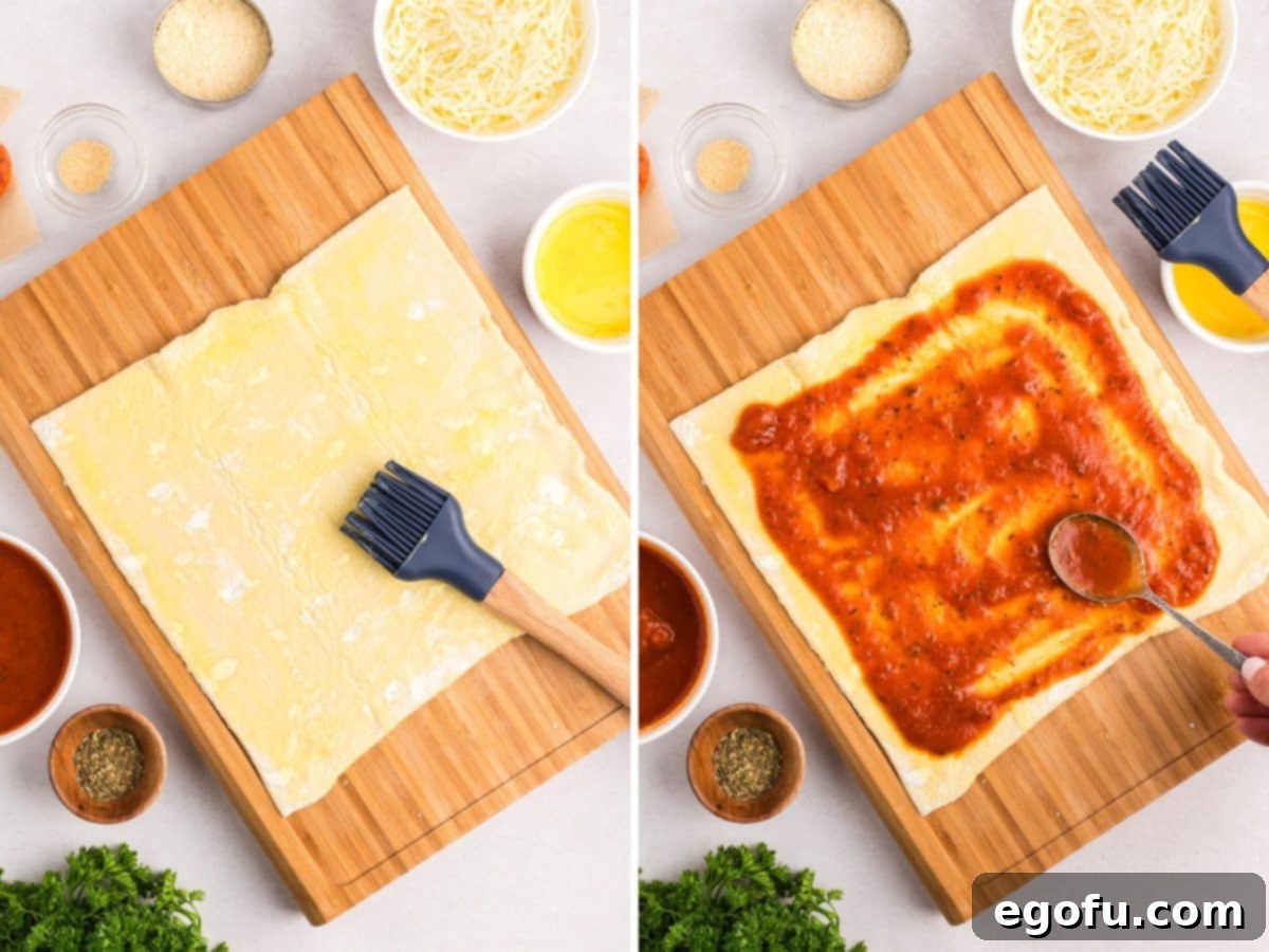 A pastry brush applies egg wash to puff pastry, followed by marinara sauce being spread evenly over the pastry, leaving a border.
