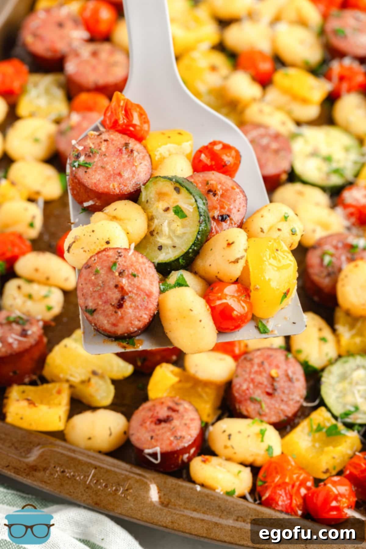 One-Pan Sausage and Gnocchi Bake 8 A serving spatula is scooping a portion of the Sheet Pan Sausage and Gnocchi directly from the baking sheet, highlighting the steam and freshness of the meal.