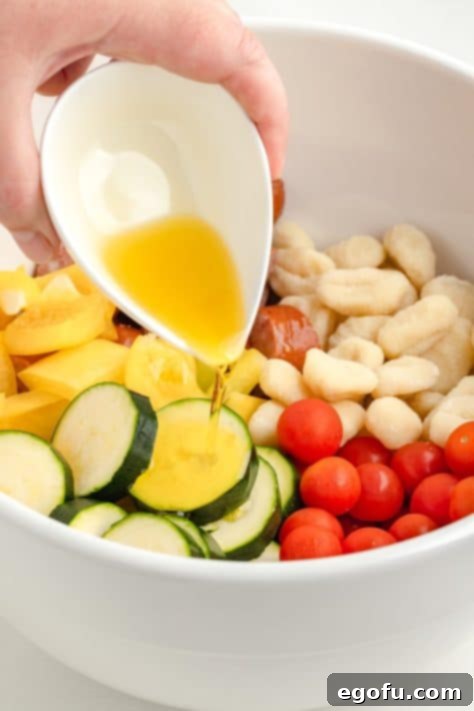 One-Pan Sausage and Gnocchi Bake 10 Olive oil being drizzled over a large bowl of veggies.