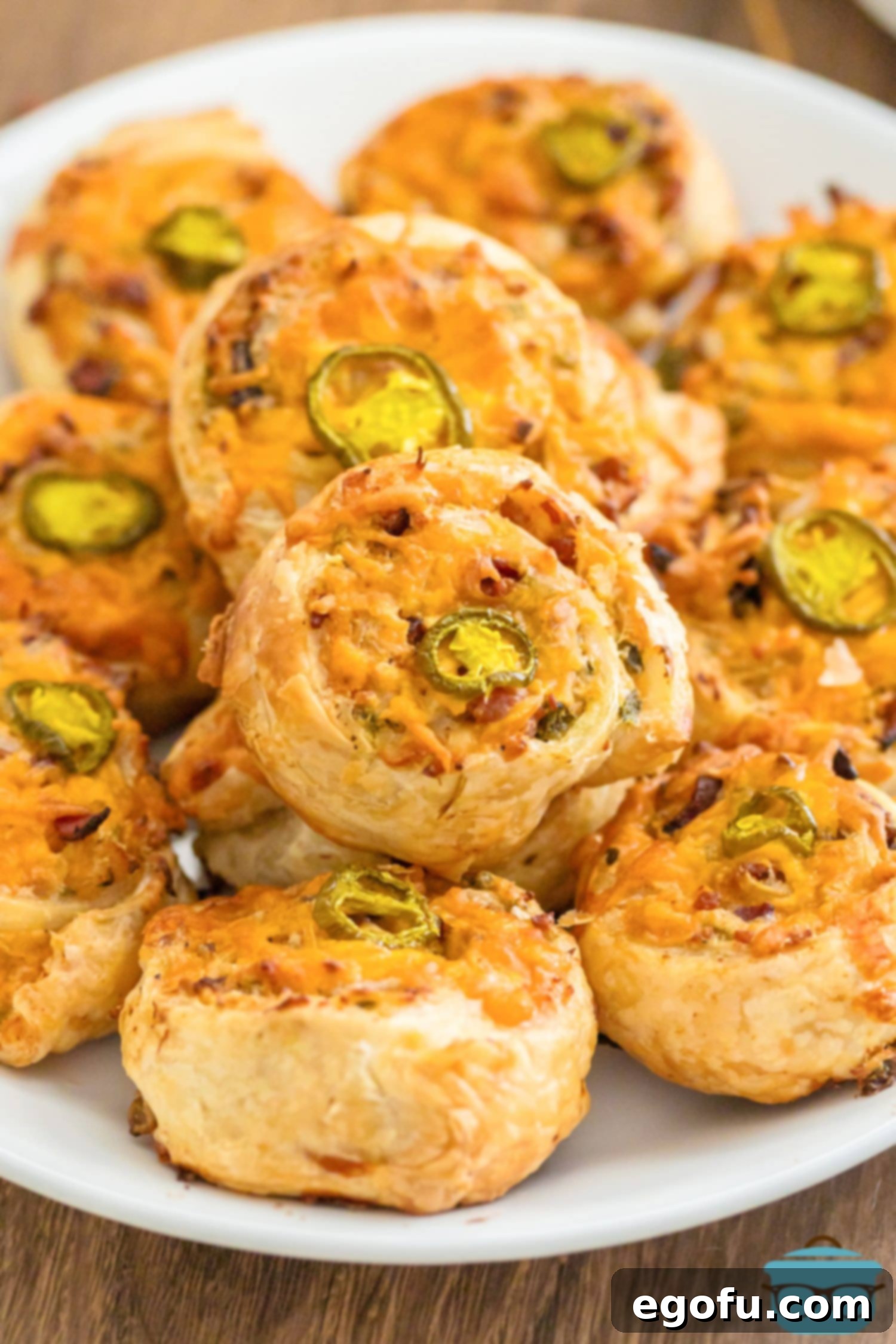 A small pile of golden-brown Baked Jalapeno Popper Pinwheels on a rustic serving platter, garnished with fresh herbs.