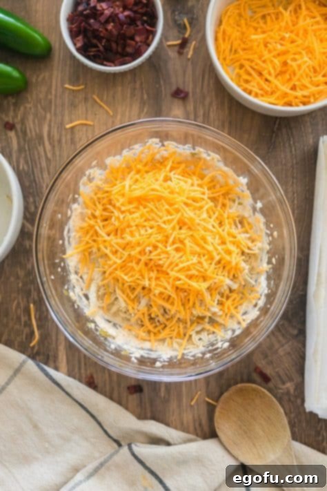 Chicken and cheese being added to cream cheese, jalapenos, onion powder, garlic powder, seasoned salt, poultry seasoning, and chili powder in a bowl.