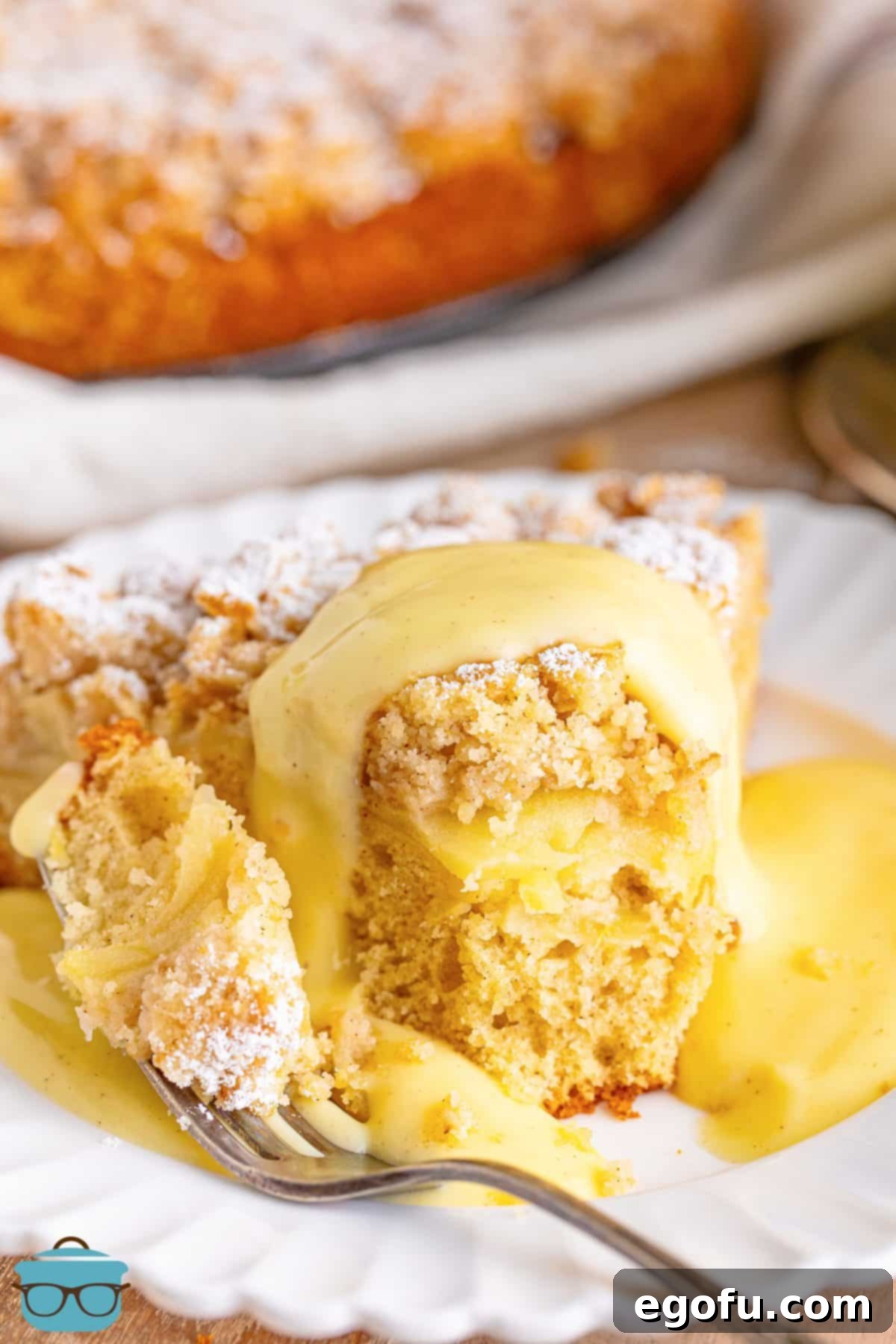 A slice of Irish Apple Cake on a plate with a fork, drizzled with creamy custard sauce.