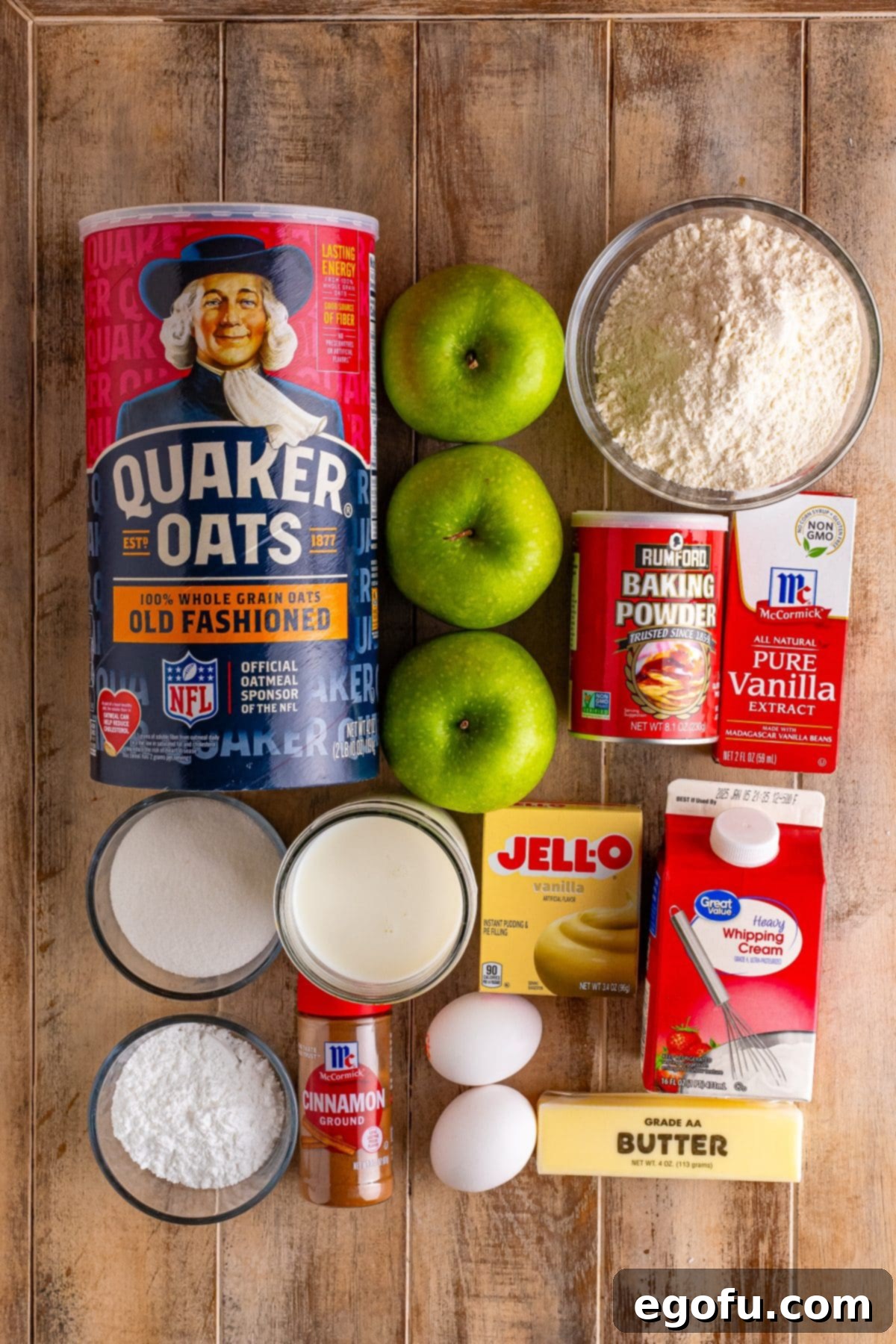 Individual ingredients for Irish Apple Cake including rolled oats, powdered sugar, granny smith apples, butter, eggs, flour, vanilla extract, baking powder, cinnamon, sugar, heavy cream, vanilla pudding, and whole milk.