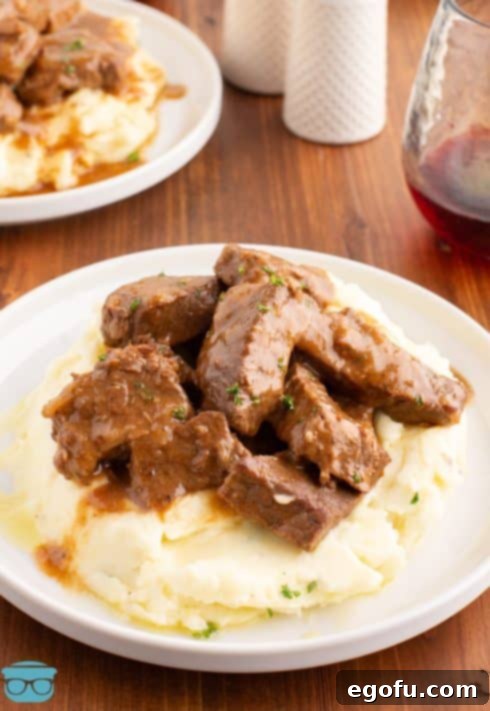 A few Beef Tips and gravy on top of a pile of mashed potatoes.