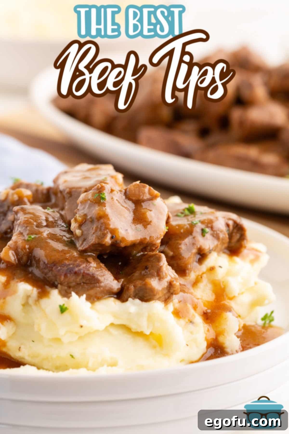 A pile of Beef Tips on top of a pile of mashed potatoes.