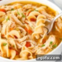 Looking closely down on a bowl of Instant Pot Chicken Noodle Soup, garnished with fresh herbs.