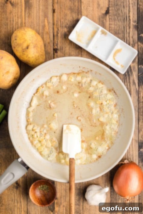 Minced garlic cloves added to the pan with softened onions and butter, being stirred to release their aromatic fragrance.
