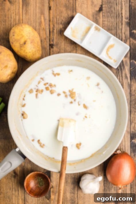 Milk being slowly added to the roux in a pan, as it's whisked to create a smooth, creamy base for the soup.