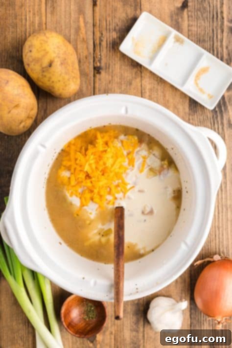 The cheese and creamy milk mixture being added to the cooked soup in the slow cooker and stirred until fully incorporated and melted.