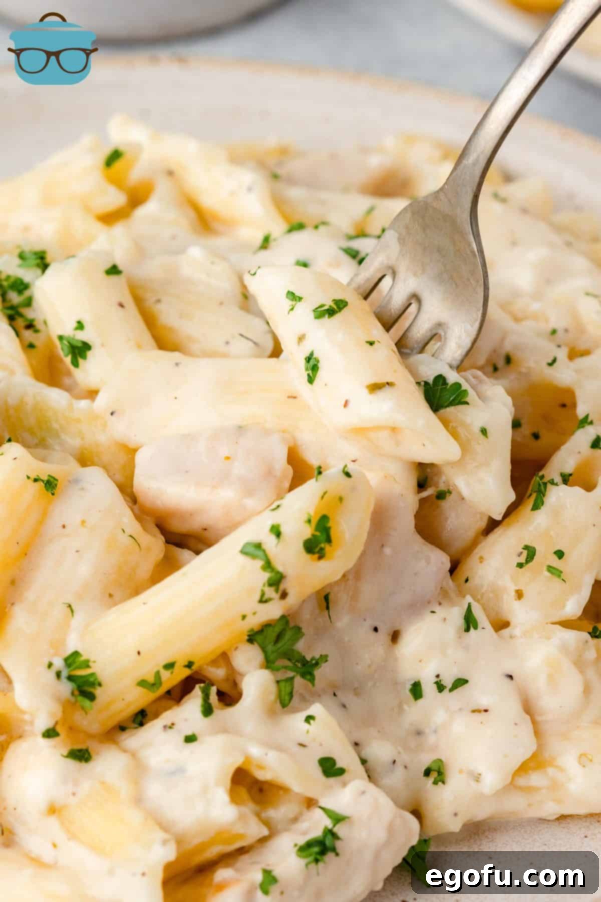 A fork getting a bite of Chicken Alfredo Casserole, showcasing creamy sauce, chicken, and pasta.