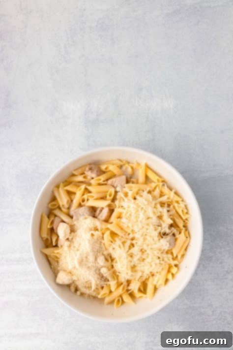 Parmesan and mozzarella cheese being added to the sauce-coated pasta and chicken mixture.