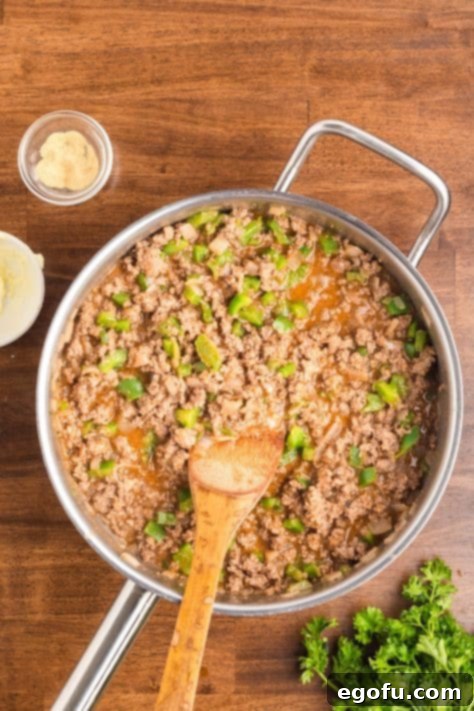A skillet with beef, onions, peppers, beef broth, ketchup, Worcestershire sauce, dried ingredients, remainder of the garlic powder, and cornstarch.