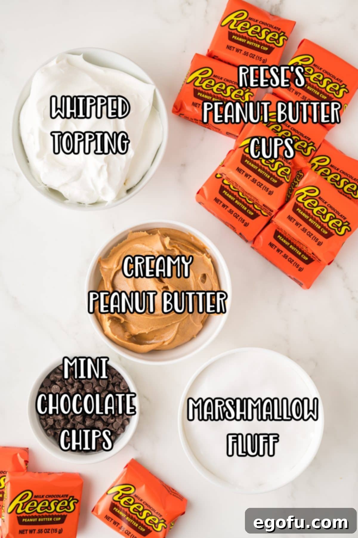 An array of ingredients laid out on a surface: creamy peanut butter, Reese's Peanut Butter Cups, mini chocolate chips, marshmallow creme, and a tub of whipped topping.