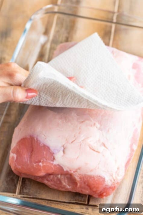 A hand with a paper towel patting a roast dry.