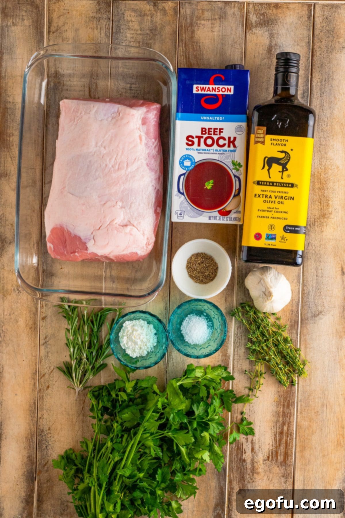 Individual ingredients laid out: pork roast, beef stock, rosemary, thyme, salt, garlic, parsley, olive oil, pepper, and cornstarch.