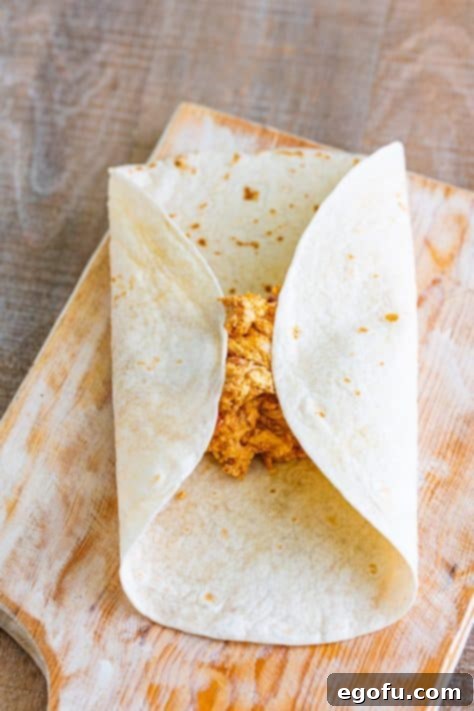 A flour tortilla being carefully folded over a chicken filling, demonstrating the technique for wrapping a chimichanga.