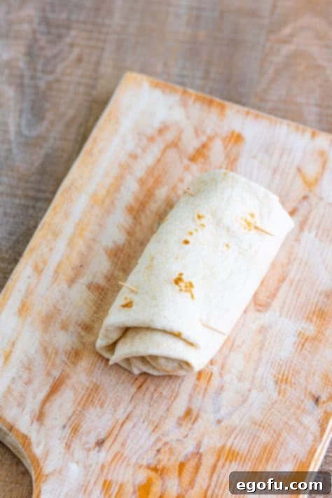 A rolled flour tortilla secured with two toothpicks, indicating it's ready for the next cooking stage.