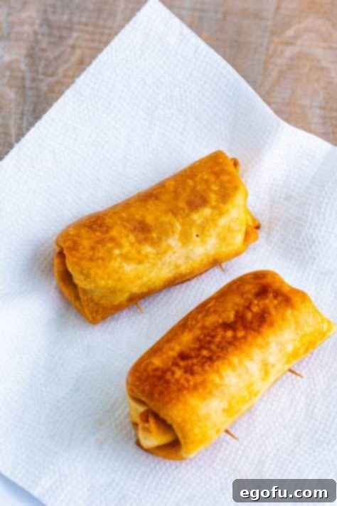 Freshly fried chimichangas resting on paper towels to drain excess oil, showing their appetizing golden color.