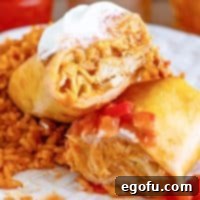 A perfectly golden, cut-open Chicken Chimichanga, revealing its rich, savory filling of chicken, beans, and cheese, on a white plate.