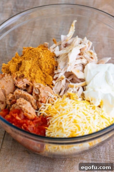 Chicken, shredded cheese, taco seasoning, refried beans, and sour cream mixed in a bowl, ready for chimichanga filling.