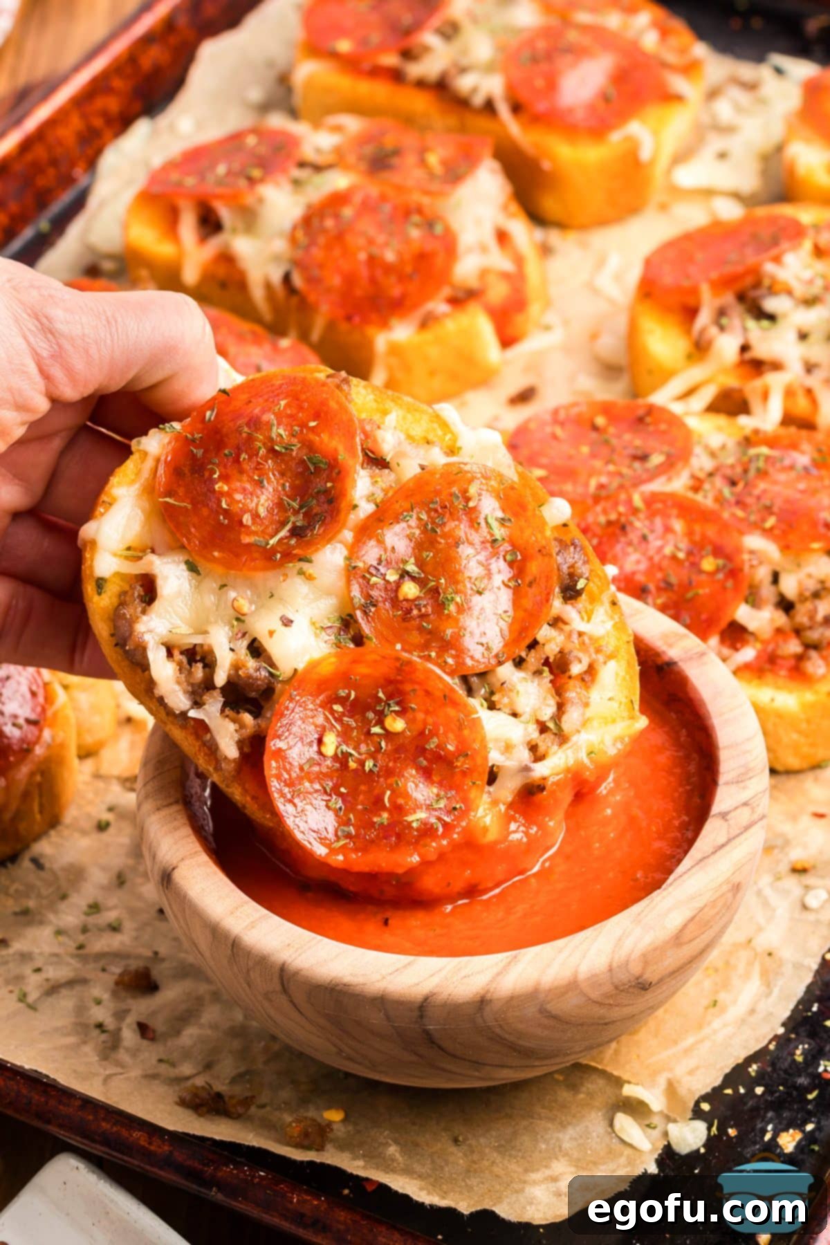 A hand dipping a crispy Garlic Texas Toast Pizza into a small bowl of warm pizza sauce.