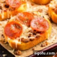 Close up looking at a piece of Garlic Texas Toast Pizza on a piece of parchment paper, with a golden crust and melted cheese.