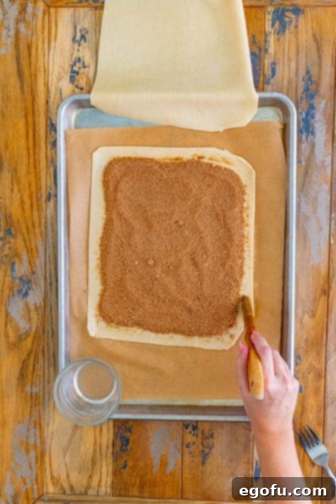 A hand brushing water along the edges of a pie crust with filling.