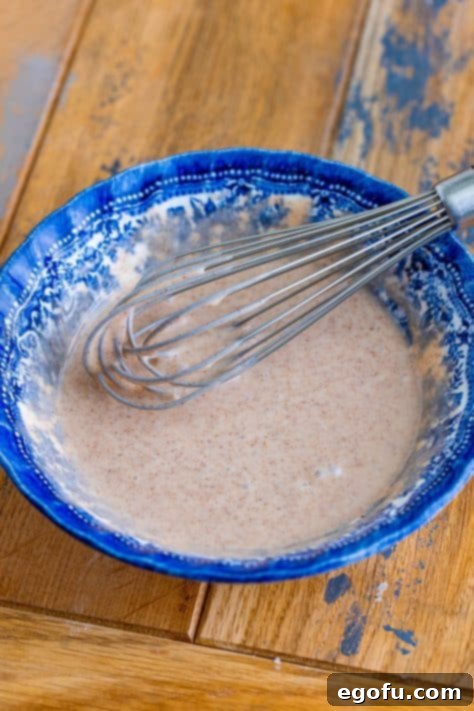 A whisk in a bowl of cinnamon sugar glaze.
