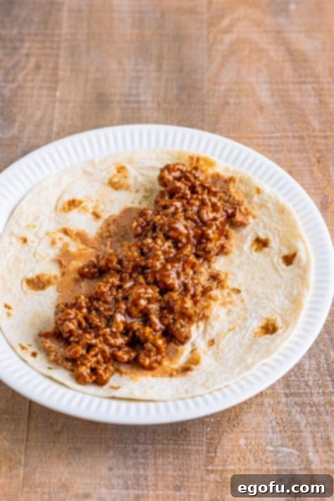 Refried beans and seasoned meat mixture layered on a tortilla, ready for the next step.