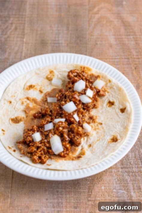 A tortilla generously filled with beans, meat, and fresh diced onions.
