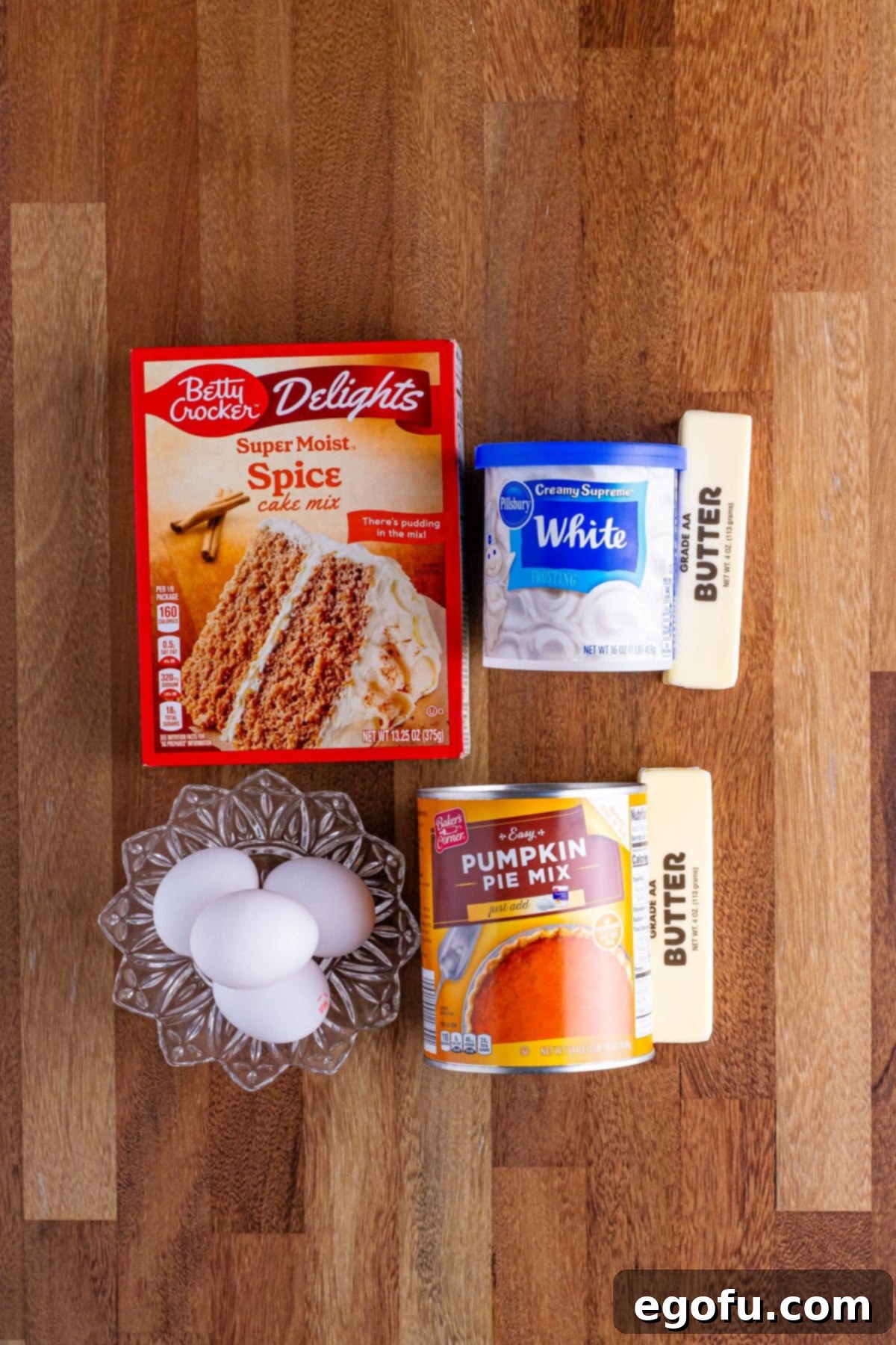 Decadent Pumpkin Pie Cake 4 Arrangement of essential ingredients for Pumpkin Pie Cake: pumpkin pie mix can, spice cake mix box, vanilla frosting container, eggs, and melted butter.
