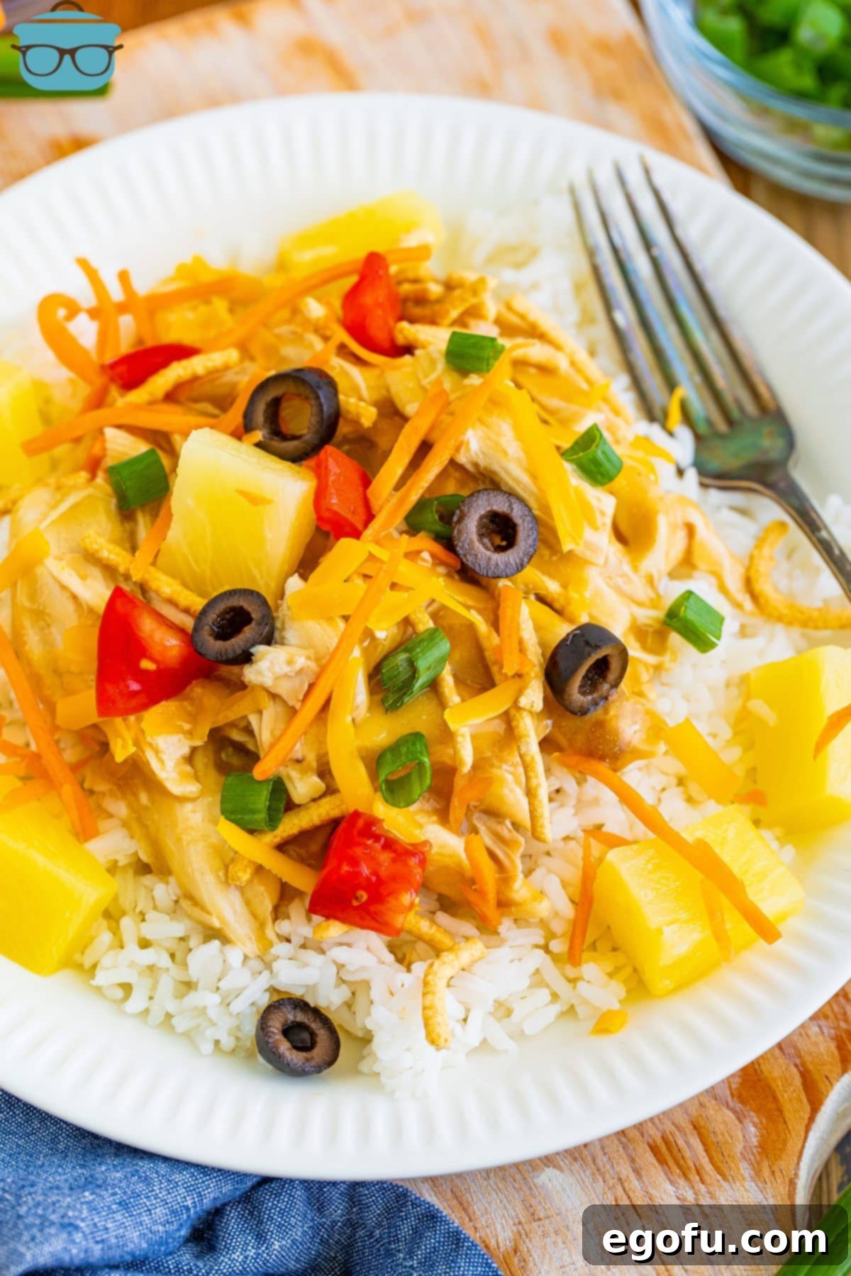 Island Topping Towers 2 Looking down on a fork and plate full of Hawaiian Haystacks, showcasing the layers of fluffy rice, creamy chicken, and a colorful assortment of fresh and crunchy toppings.