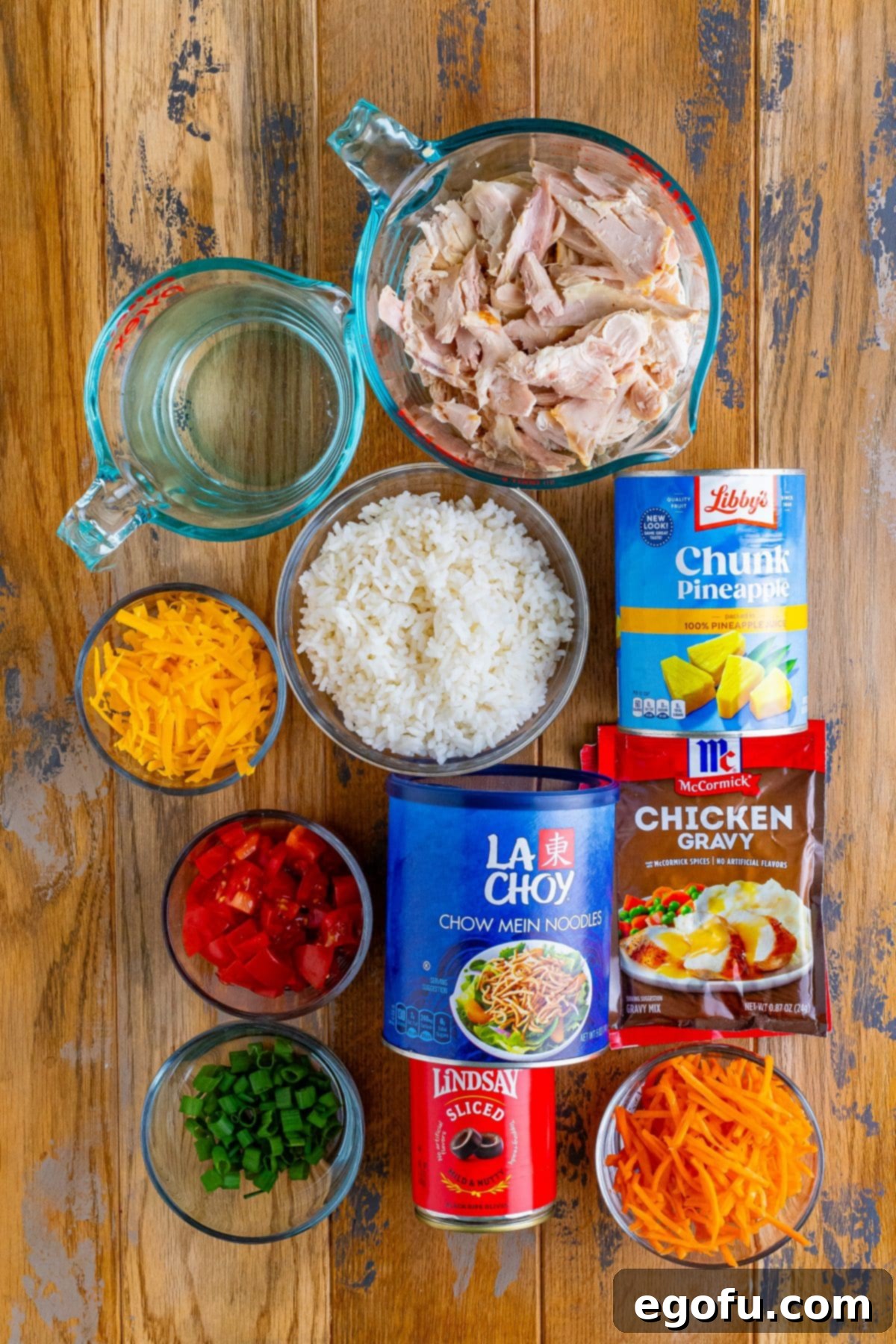 Island Topping Towers 4 A vibrant flat lay of all the fresh and packaged ingredients needed for Hawaiian Haystacks, including chicken gravy mix, shredded chicken, rice, and various colorful toppings like pineapple, chow mein noodles, green onion, carrots, cheese, tomato, and black olives, neatly arranged.