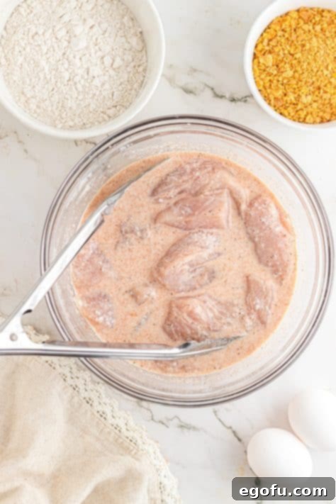 Chicken marinating in a bowl with tongs.