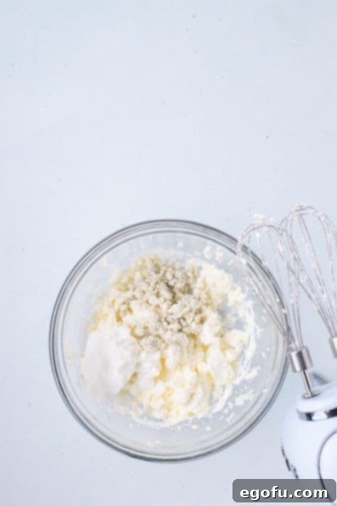 Blue cheese and mayo being added to cream cheese in a bowl.