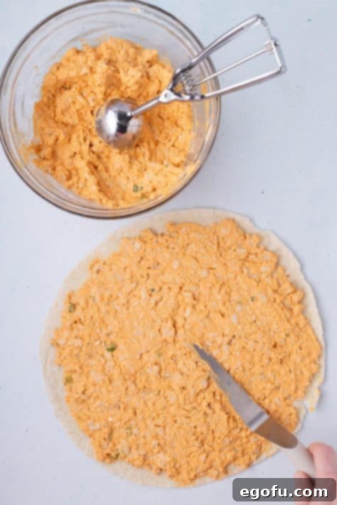 Buffalo chicken mixture being spread over tortillas.